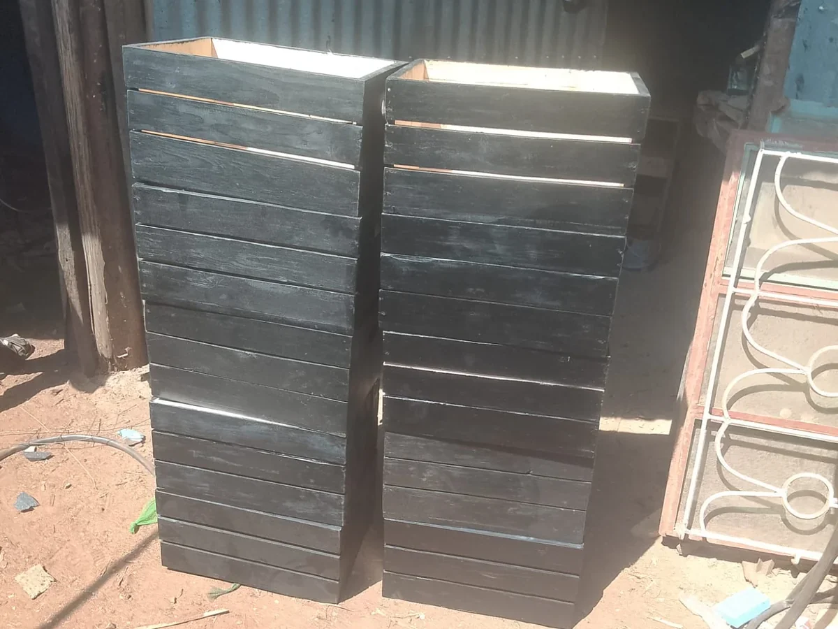 Tall stacked columns of black-painted slatted wooden crates in Kangundo workshop yard.